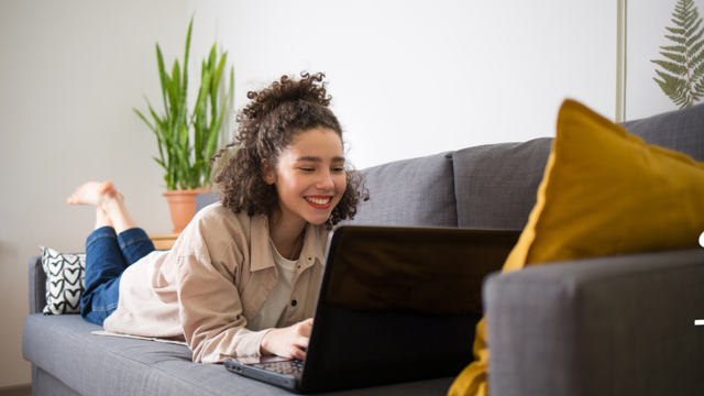 Woman lying on couch on her laptop thinking about a personal loan