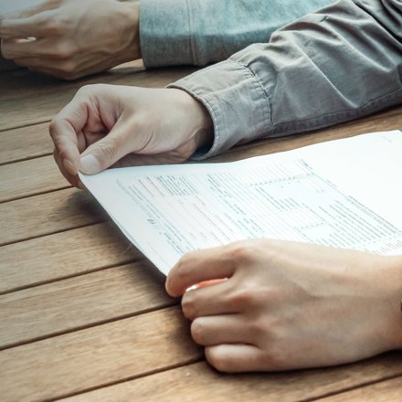Hands holding a printed form at a wooden table, reading it closely