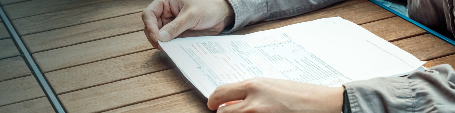 Hands holding a printed form at a wooden table, reading it closely