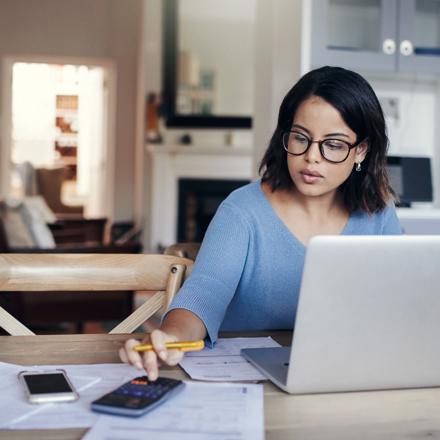 Woman in blue top on laptop computer and calculator working out her financial health
