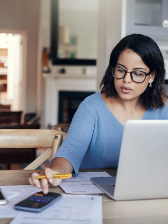 Woman in blue top on laptop computer and calculator working out her financial health