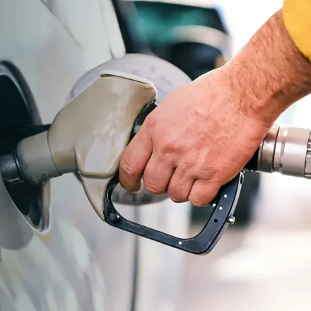 Hand holding a fuel nozzle while filling up a car at a petrol station