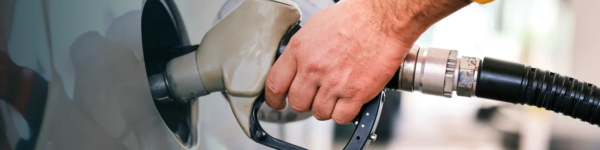 Hand holding a fuel nozzle while filling up a car at a petrol station