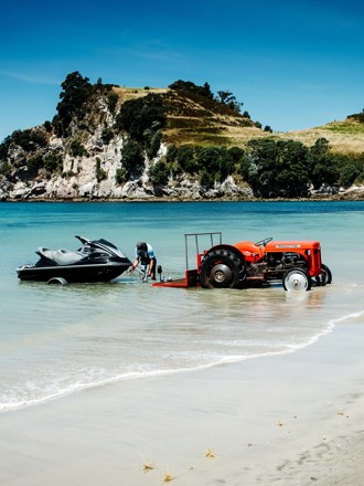 Jet ski being launched from a trailer by a tractor at a sunny New Zealand beach