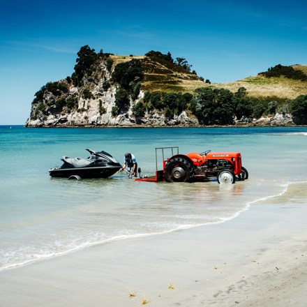 Jet ski being launched from a trailer by a tractor at a sunny New Zealand beach