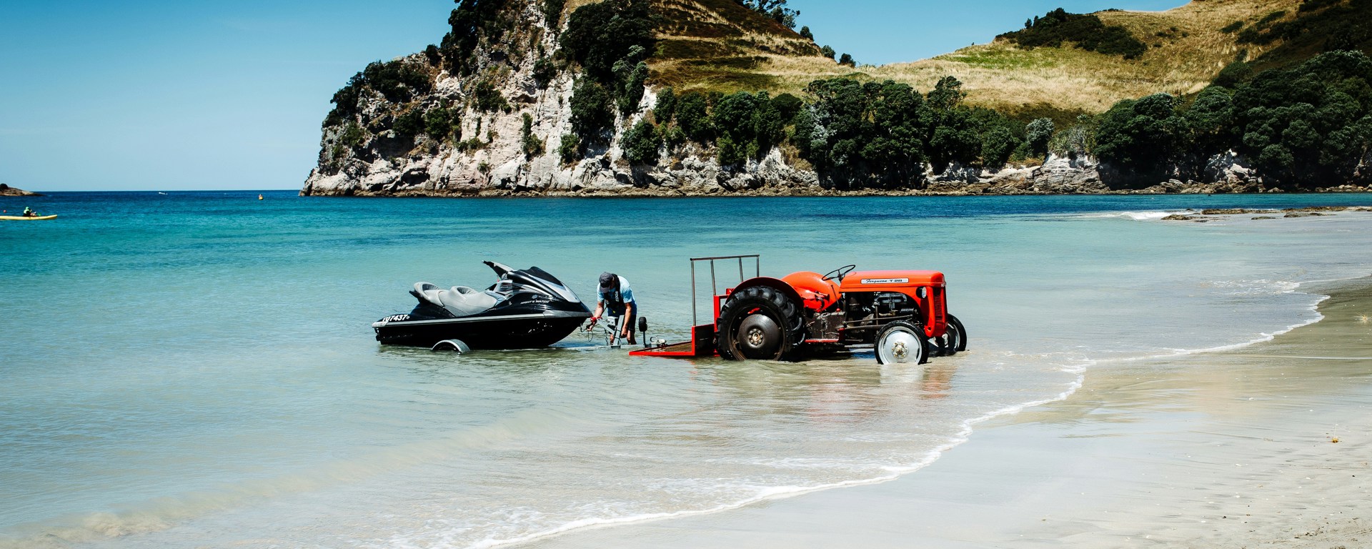 Jet ski being launched from a trailer by a tractor at a sunny New Zealand beach